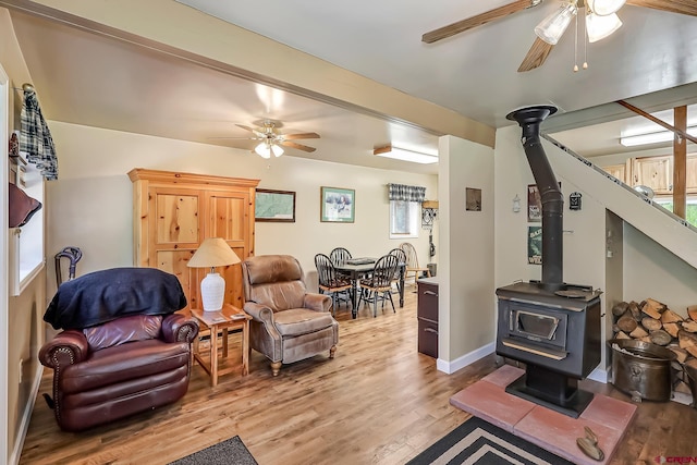 living room with light hardwood / wood-style floors, a wood stove, a wealth of natural light, and ceiling fan