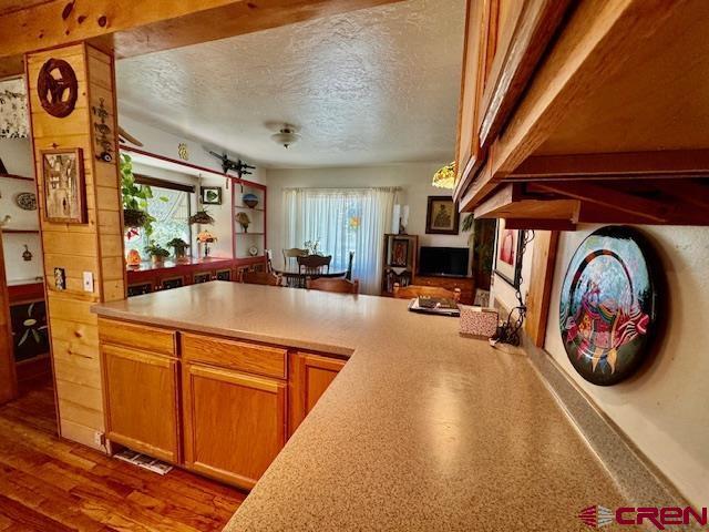 kitchen with a textured ceiling, kitchen peninsula, hardwood / wood-style floors, and beam ceiling