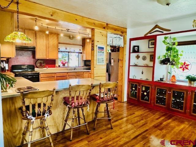 kitchen with kitchen peninsula, range, decorative light fixtures, sink, and dark hardwood / wood-style floors