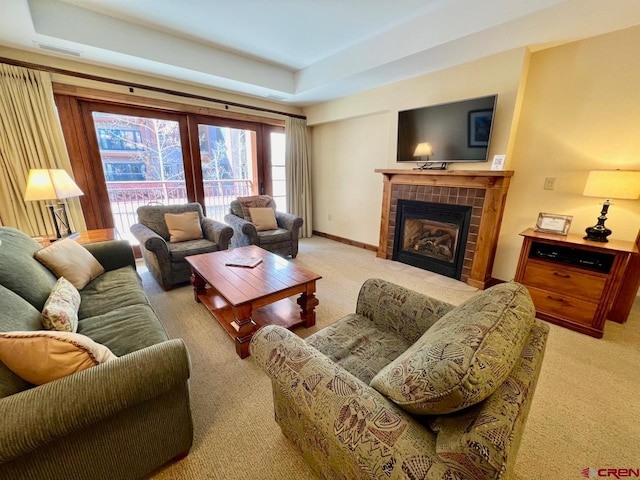 living room with light carpet, a tiled fireplace, and a raised ceiling