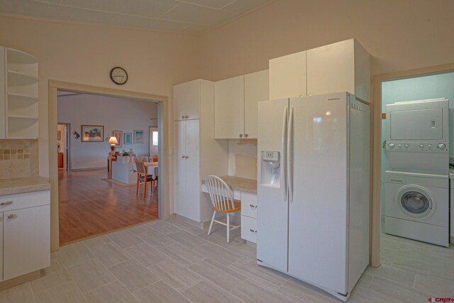 kitchen with stacked washing maching and dryer, white fridge with ice dispenser, white cabinets, and light hardwood / wood-style flooring