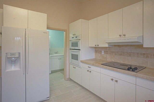 kitchen featuring white cabinetry, light tile patterned flooring, backsplash, and white appliances