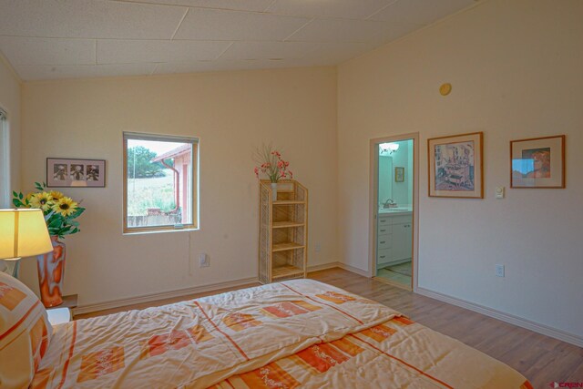 bedroom with vaulted ceiling, ensuite bathroom, and light wood-type flooring