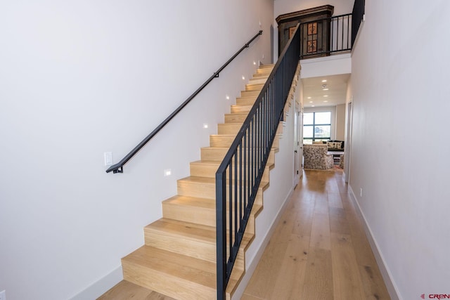 stairway featuring light wood-type flooring and a high ceiling