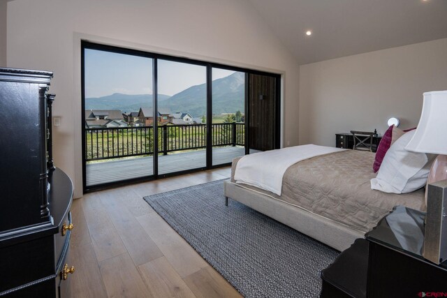 bedroom with a mountain view, light hardwood / wood-style floors, access to exterior, and high vaulted ceiling