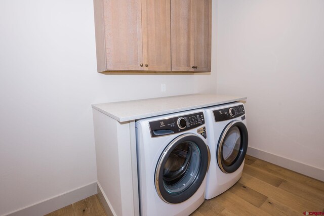 clothes washing area featuring washing machine and dryer, light hardwood / wood-style flooring, and cabinets