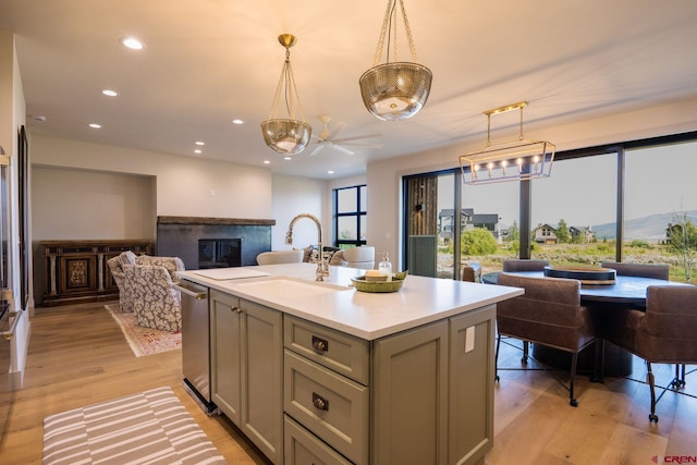 kitchen with decorative light fixtures, light wood-type flooring, sink, dishwasher, and a center island with sink