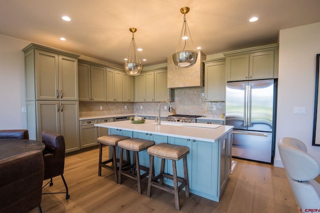 kitchen with decorative backsplash, stainless steel built in refrigerator, light wood-type flooring, and an island with sink