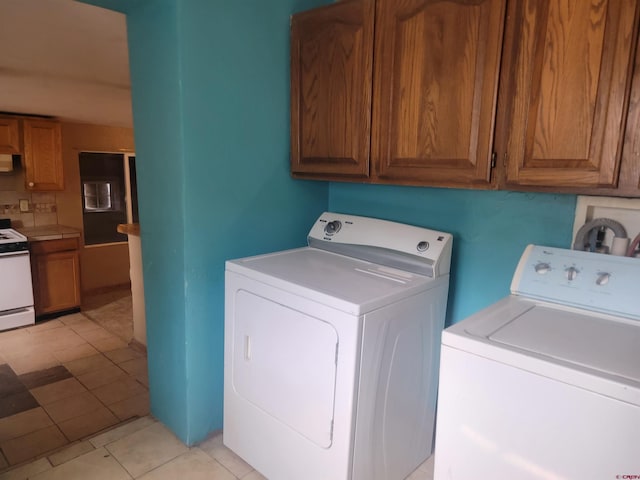 clothes washing area featuring cabinets, washing machine and dryer, and light tile patterned floors