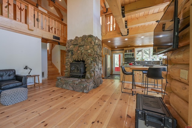 living room with wood ceiling, a wood stove, light wood-type flooring, beamed ceiling, and a towering ceiling