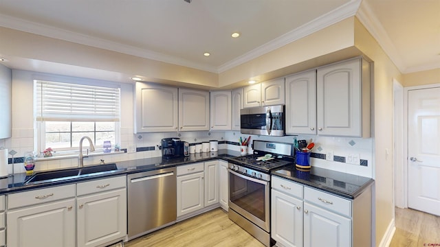 kitchen featuring light wood-style flooring, a sink, ornamental molding, appliances with stainless steel finishes, and dark countertops