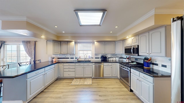 kitchen featuring appliances with stainless steel finishes, light wood-style floors, ornamental molding, a sink, and a peninsula