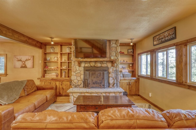 living area featuring baseboards, a textured ceiling, a stone fireplace, light wood-style floors, and built in shelves