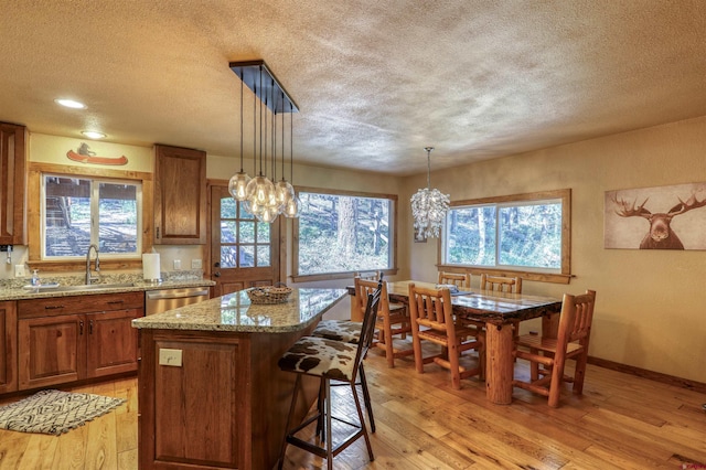 kitchen with brown cabinets, hanging light fixtures, a kitchen island, a sink, and dishwasher