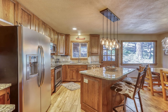 kitchen featuring a center island, hanging light fixtures, appliances with stainless steel finishes, brown cabinetry, and a sink