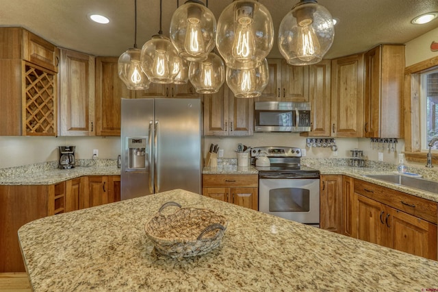 kitchen featuring stainless steel appliances, hanging light fixtures, light stone counters, and a sink