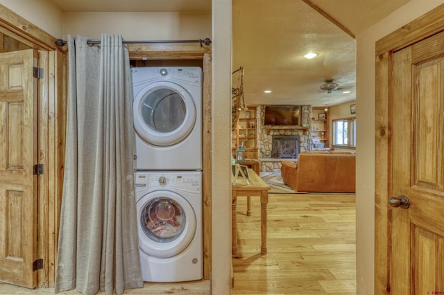 clothes washing area featuring laundry area, wood finished floors, a textured ceiling, a stone fireplace, and stacked washing maching and dryer