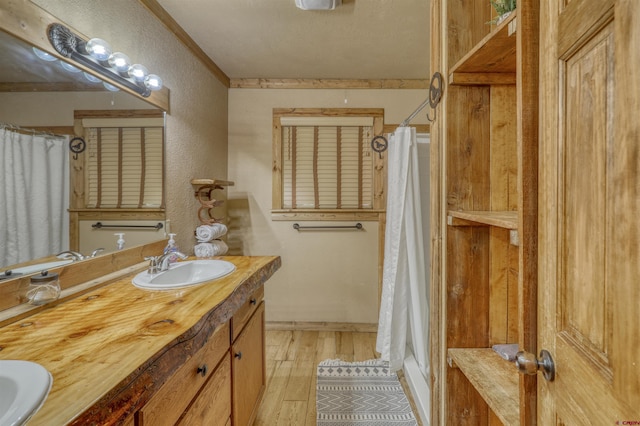 full bath featuring double vanity, a textured wall, a sink, and wood finished floors