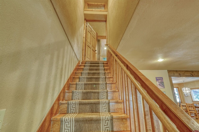 staircase featuring a chandelier, visible vents, a textured ceiling, and wood finished floors