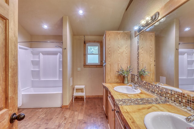 full bath featuring double vanity, shower / tub combination, a sink, and wood finished floors