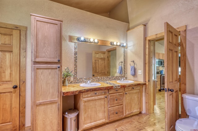 full bath with double vanity, a sink, toilet, and decorative backsplash