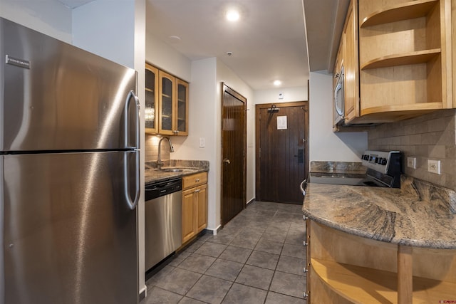 kitchen with sink, appliances with stainless steel finishes, dark tile patterned flooring, decorative backsplash, and dark stone counters