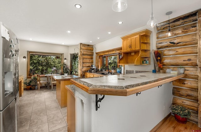 kitchen with a healthy amount of sunlight, a kitchen bar, log walls, decorative light fixtures, and kitchen peninsula