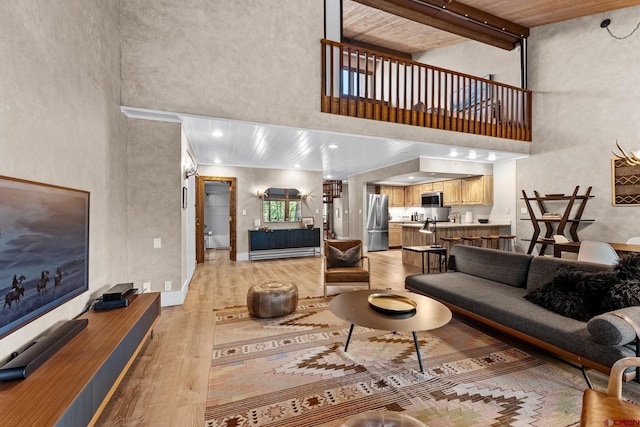 living room with beam ceiling, a high ceiling, wooden ceiling, and light hardwood / wood-style floors