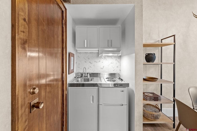 kitchen with sink, white cabinetry, stainless steel counters, hardwood / wood-style flooring, and backsplash