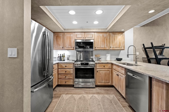 kitchen with sink, light stone counters, light wood-type flooring, appliances with stainless steel finishes, and a tray ceiling