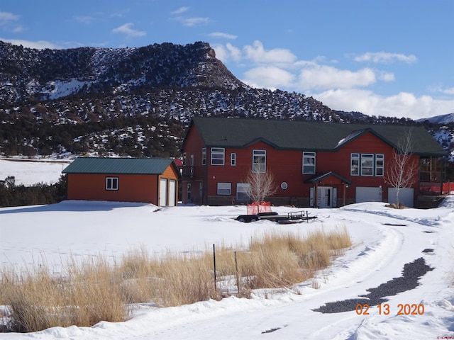 snow covered back of property featuring a mountain view, a garage, and an outdoor structure