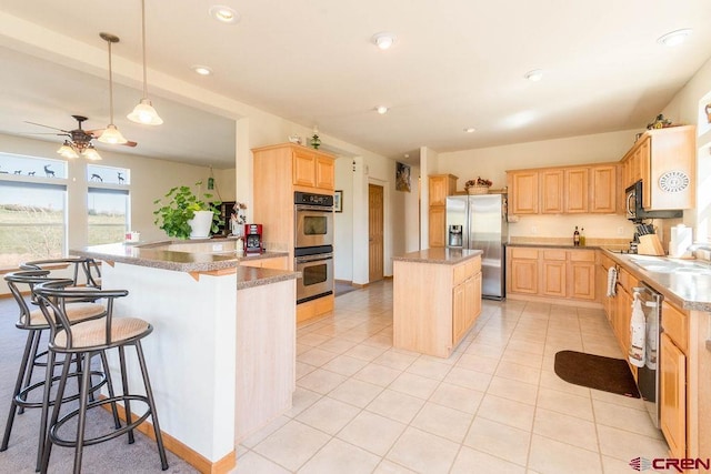 kitchen featuring appliances with stainless steel finishes, a breakfast bar, light brown cabinetry, hanging light fixtures, and kitchen peninsula