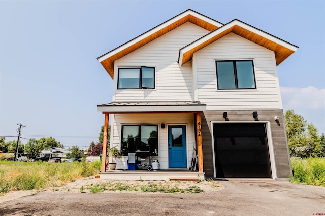 modern home with a garage, driveway, metal roof, a standing seam roof, and covered porch