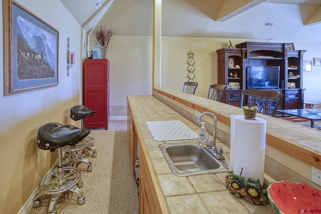 bar featuring carpet, sink, tile counters, and lofted ceiling