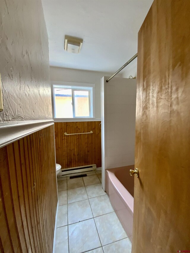 bathroom with tiled shower / bath, wood walls, a baseboard radiator, toilet, and tile patterned floors