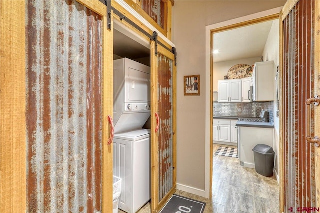 washroom featuring light wood-type flooring, stacked washer and clothes dryer, and a barn door