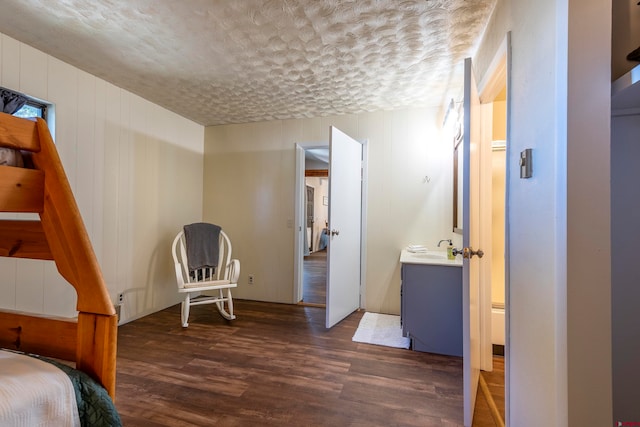 bedroom featuring dark wood-type flooring, a textured ceiling, sink, and wooden walls