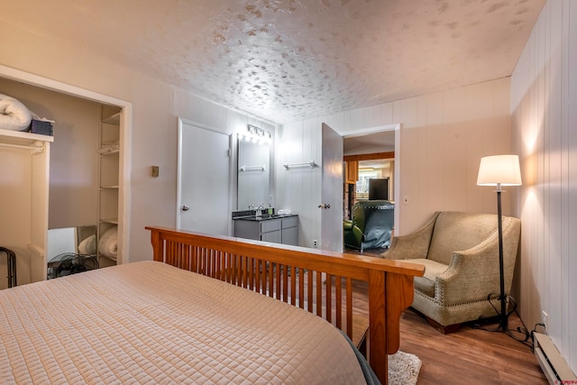 bedroom featuring a textured ceiling, baseboard heating, wooden walls, and hardwood / wood-style flooring