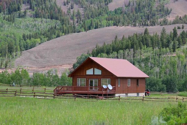 view of front facade with a wooden deck, a front lawn, and a rural view