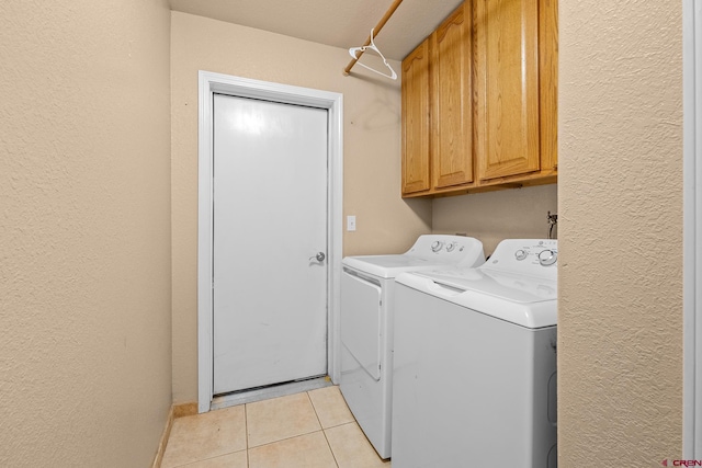 laundry room featuring cabinet space, a textured wall, washer and clothes dryer, and light tile patterned flooring