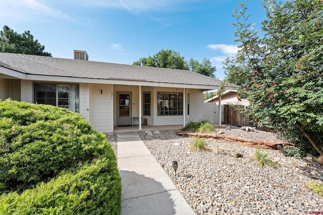 ranch-style home featuring covered porch, roof with shingles, and fence