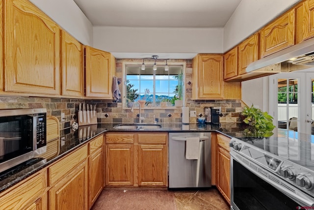 kitchen with under cabinet range hood, stainless steel appliances, a sink, decorative backsplash, and dark stone countertops