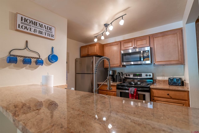 kitchen with appliances with stainless steel finishes, light stone countertops, and rail lighting