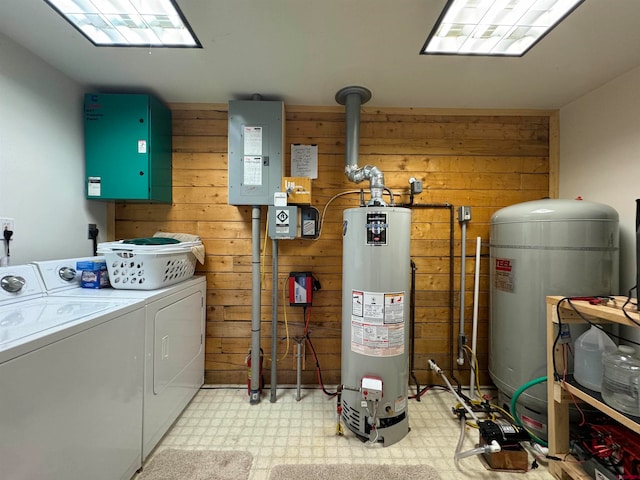 washroom featuring wooden walls, electric panel, washer and clothes dryer, and gas water heater