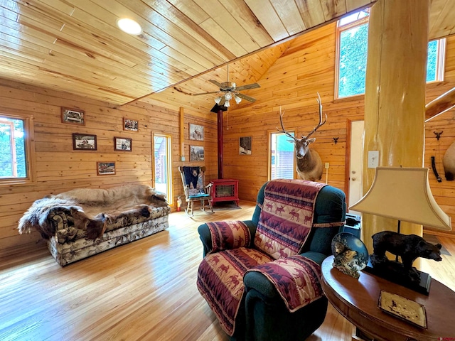 living room with wood ceiling, wooden walls, vaulted ceiling, light hardwood / wood-style floors, and a wood stove