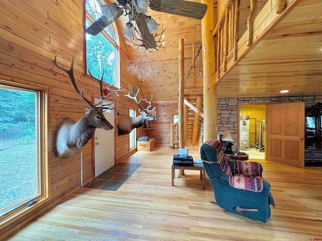 living room featuring ceiling fan, a towering ceiling, light hardwood / wood-style flooring, and wooden walls