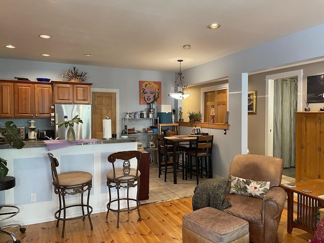 kitchen featuring stainless steel fridge, light wood-type flooring, a breakfast bar, and pendant lighting