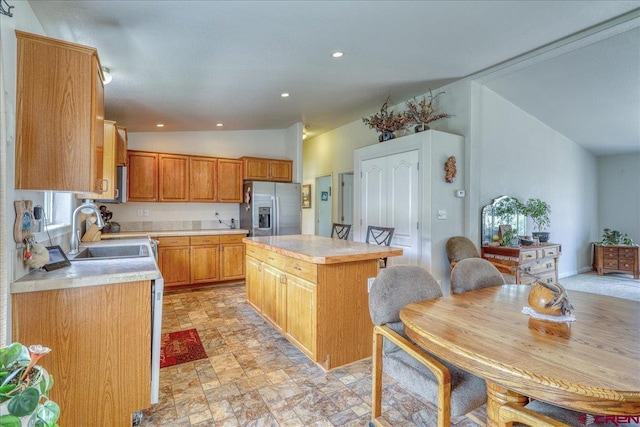 kitchen with a sink, vaulted ceiling, light countertops, a center island, and stainless steel fridge