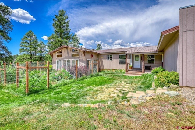 rear view of property featuring metal roof, a yard, fence, and a garden