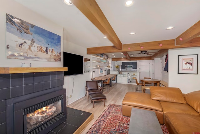 living room with beamed ceiling, ceiling fan, light hardwood / wood-style flooring, and a tiled fireplace